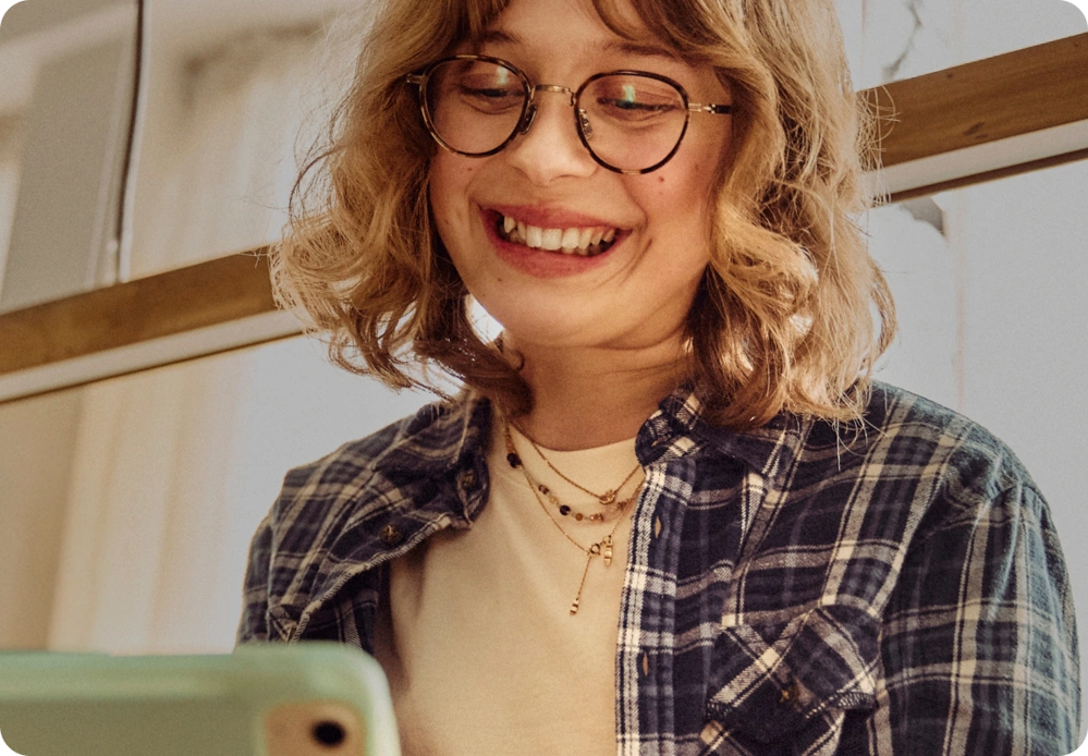 Smilende person med briller bruger mobiltelefon i hyggelige og lyse omgivelser.