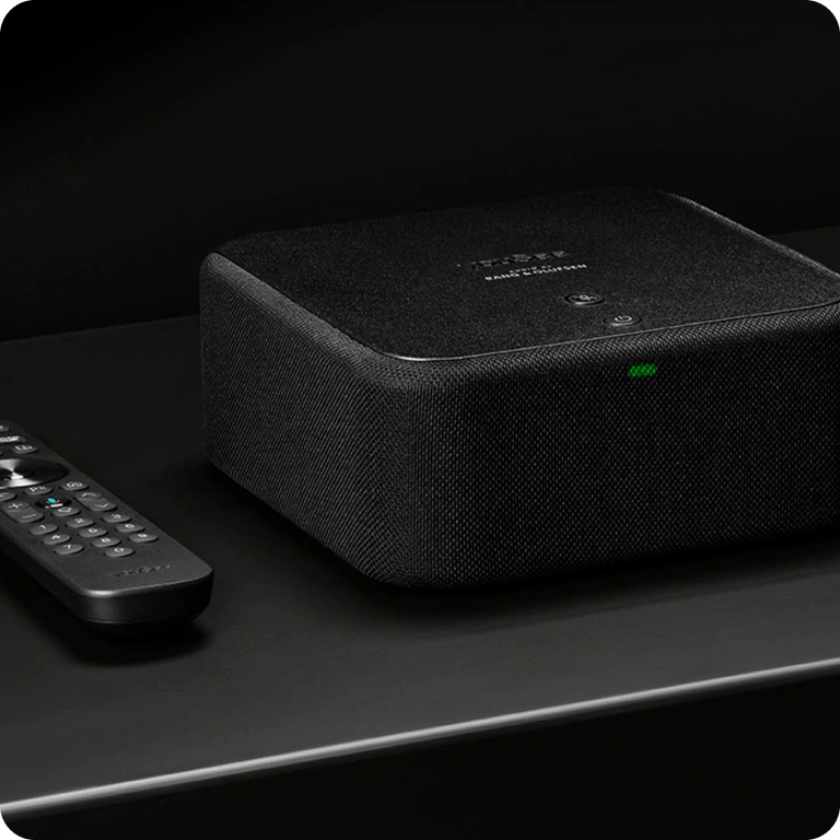 YouSee Audio og fjernbetjening placeret på mørk overflade i stilrent produktfoto.